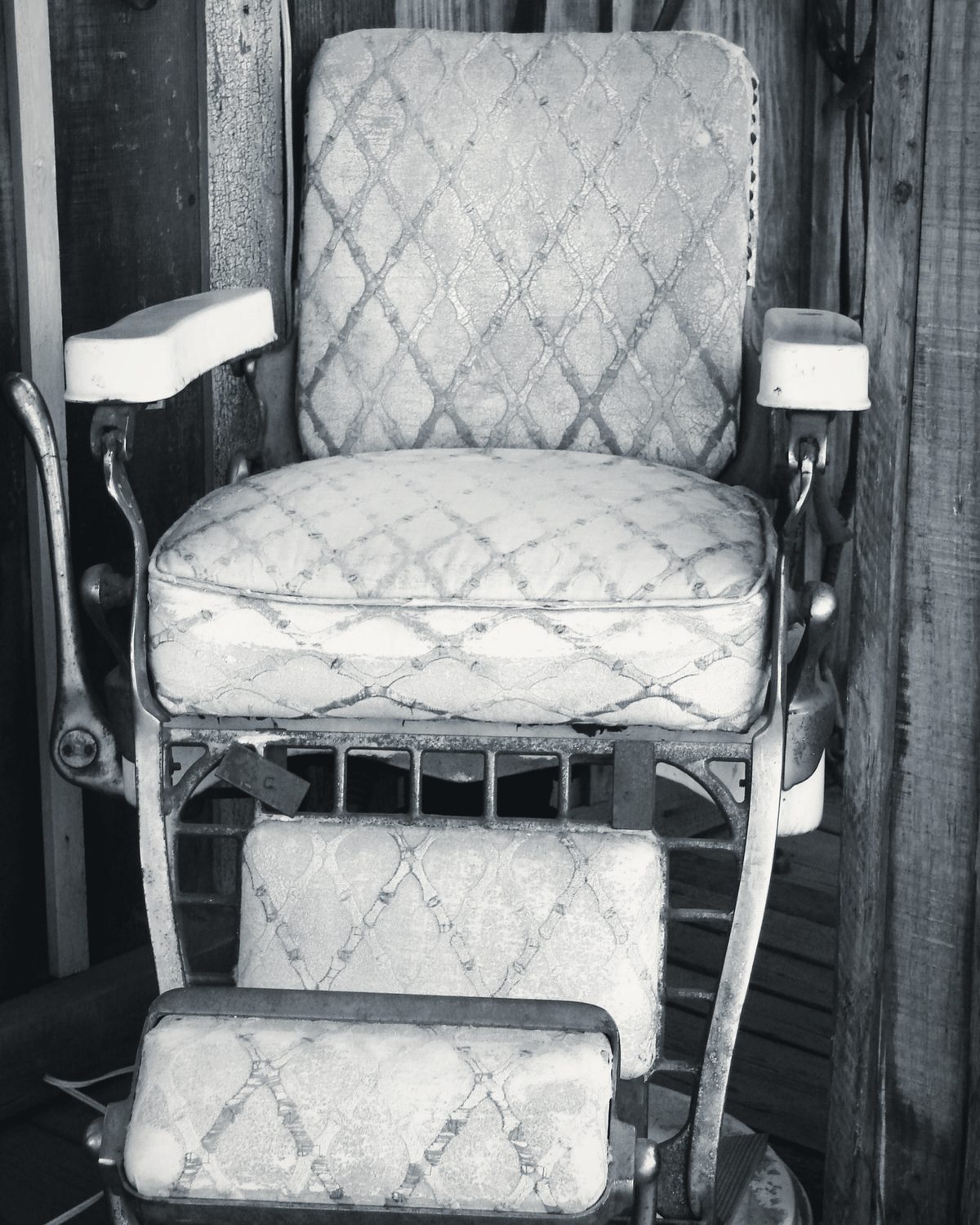 An antique barber chair with white porcelain armrests, a nickel-plated frame and a patterned seat and footrest