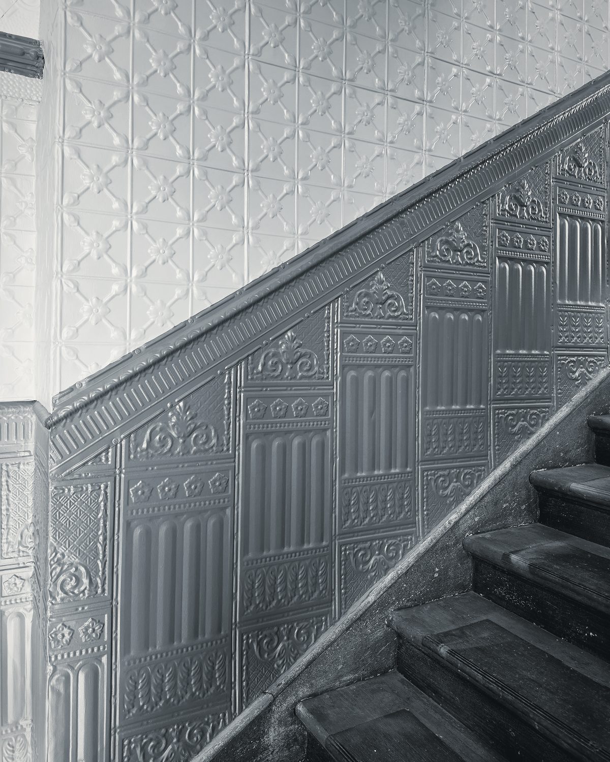 A narrow stairwell walled in embossed pressed tin, worn wooden treads climbing to the right